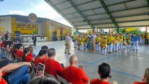 Apresentação de banda de percussão e instrumentos de sopro em evento dos Amigos do Bem, com plateia de voluntários assistindo.